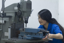 Young Woman Using Drill In Industrial Workshop