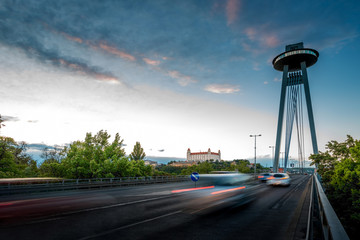 View on the Modern bridge with observation deck and restaurant called UFO and castle in Bratislava city at the sunset. Long exposure technique with motion of cars