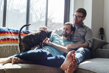 Male Couple Relaxing On Sofa Together With Cat