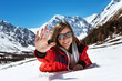 Happy attractive girl lying on the snow on mountains backdrop