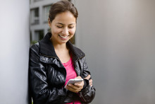 Young Woman Leaning Against Pillar Reading Smartphone Texts