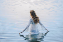 Rear View Of Young Woman Standing In Lake Rippling Surface With Her Fingers