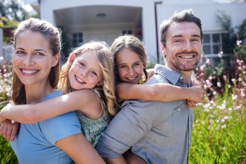 Wall Mural - Portrait of parents giving a piggy back to daughters