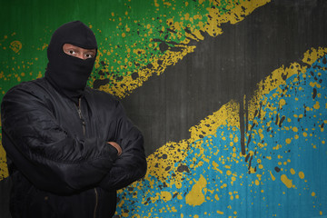 Wall Mural - dangerous man in a mask standing near a wall with painted national flag of tanzania