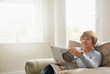 Senior Woman Sitting In Armchair Reading Magazine