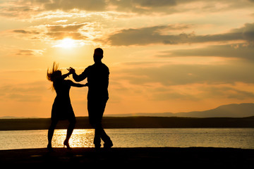 Wall Mural - Couple silhouette dancing by the sea at sunset