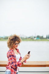 Wall Mural - Young woman standing at the balcony and using mobile phone