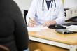 Midsection Of Doctor Writing Prescription For Patient At Desk