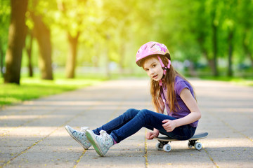 Wall Mural - Cute little preteen girl wearing helmet sitting on a skateboard