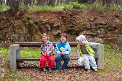 Fotografie, Obraz Children sitting on the bench laughing and having fun outdoors in the park