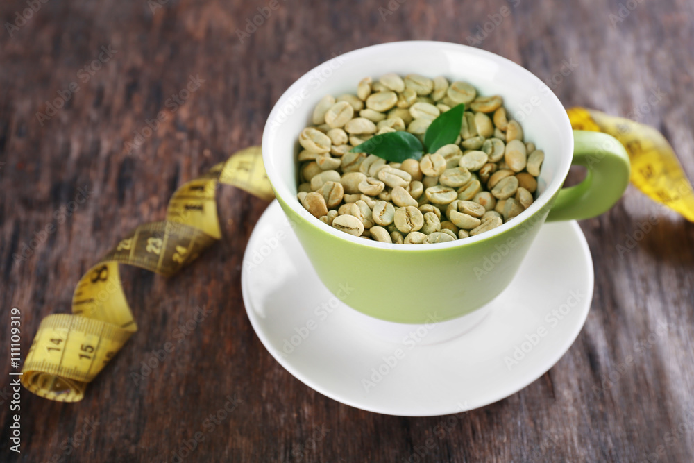 Green coffee beans in a cup with measuring tape on wooden table