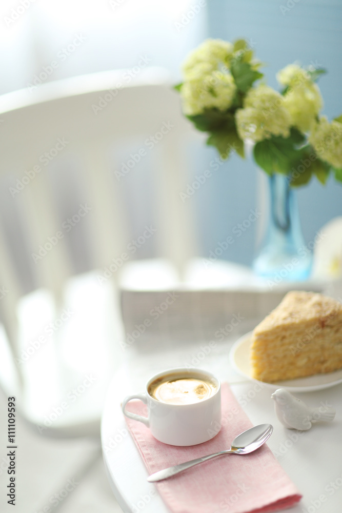Cup of coffee with cake on white table in light interior