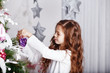 Little girl decorating christmas tree with toys and flowers.