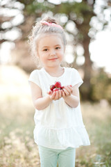 Wall Mural - Smiling baby girl 4-5 year old holding strawberry outdoors. Looking at camera. Childhood.