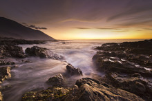 golden sunset at pacific ocean with waves on rocky shore