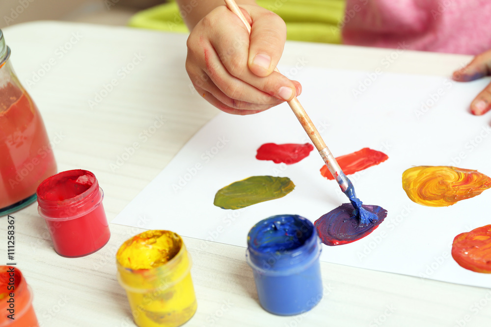 Child drawing with bright paints on paper, closeup