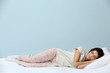 © Africa Studio - Young woman in pajamas sleeping on bed on blue background