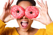 Woman holding colorful donuts against her eyes