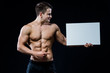 © romankosolapov - Shirtless muscular young man standing holding a blank horizontal white banner pointing finger at the copyspace for your text, on black