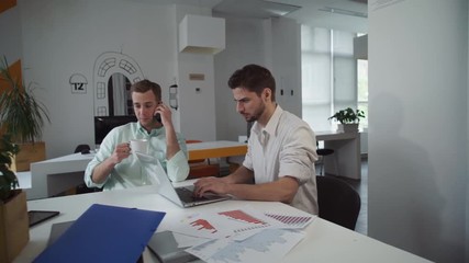 Aufkleber - Young man working with computer. Handsome adult male using app on smartphone. Casual woman brings cup of coffee for colleague 