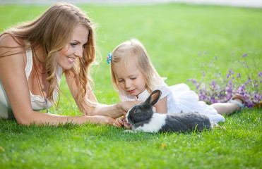 Young woman and her daughter playing with a pet rabbit in a park