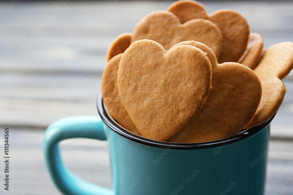 Heart shaped biscuits in metal mug on wooden background
