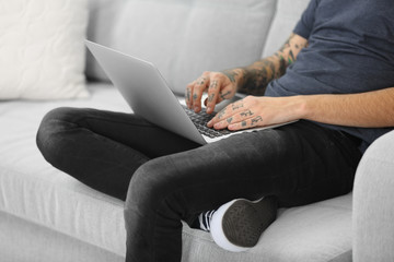 Canvas Print - Young man with tattoo using laptop on a sofa at home