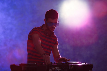 DJ playing music at mixer on colorful blurred background