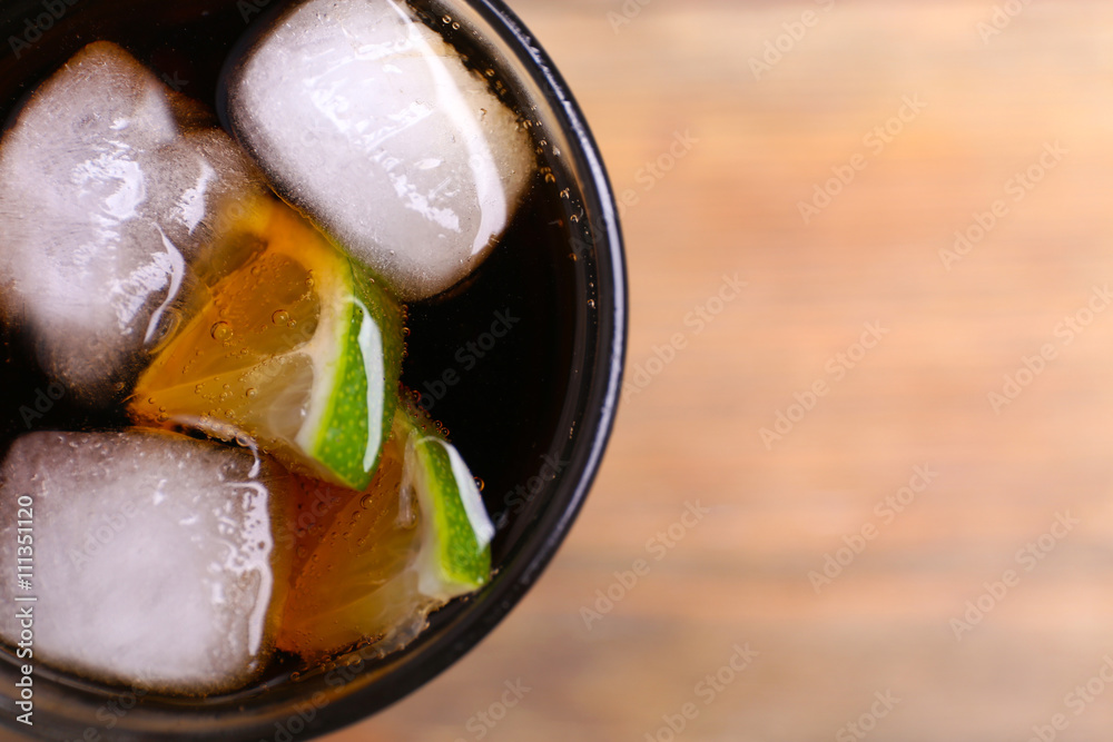 Cocktail with lime slices and ice blocks on wooden table, close up