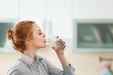 Young woman in the kitchen drinking water