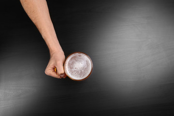 Canvas Print - Male hand holding glass of beer on dark background