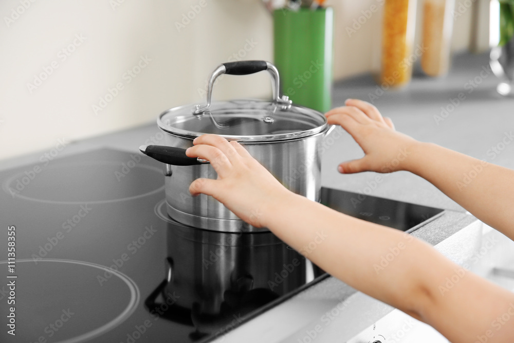 Little child playing with pan and electric stove in the kitchen