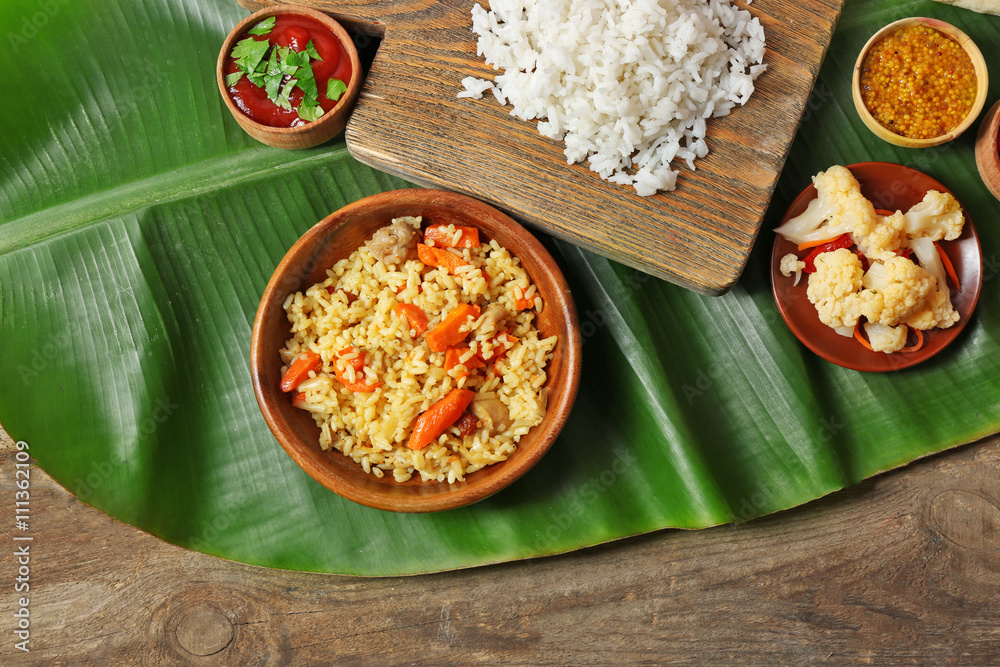 Boiled and fried rice with vegetables on banana leaf over wooden background