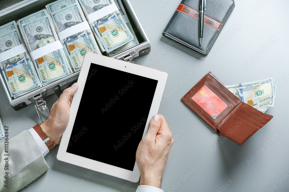 Businessman with tablet and case full of money