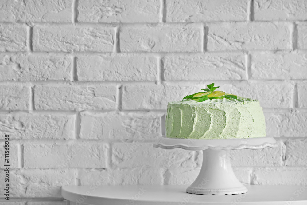 Big lime cake on a white stand beside brick wall