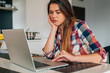 © jakubzak - Sad girl sitting i the kitchen and using laptop.