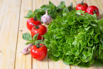 Wall Mural - Fresh lettuce, tomato, basil and garlic for a light summer salad on a wooden surface, selective focus 