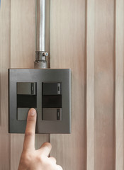 Wall Mural - A finger is turning on a grey or black metallic light switch on wooden blackground. Industrial or factory light switch with galvanize electric wire.