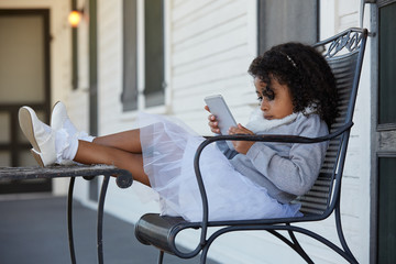 Wall Mural - Kid girl sitting in the porch playing smartphone