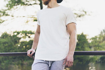 Sticker - Image Bearded Muscular Man Wearing White Empty t-shirt, snapback cap and shorts in summer holiday. Chilling time near the lake. Green City Garden Park Sunset Background. Front view. Horizontal Mockup.