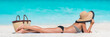 Beach summer vacation woman relaxing sunbathing on white Caribbean sand and turquoise ocean. Young tourist girl lying down on towel by sea wearing bikini and sun hat enjoying summer travel holidays.