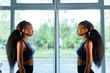 Side view of beautiful black african american young lady looking at mirror in the gym and admiring herself