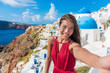© Maridav - Europe travel selfie Asian woman in Oia village, Santorini. Cute happy smiling tourist girl taking self-portrait picture with smartphone during summer vacation in famous European destination, Greece.