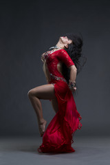 Young beautiful exotic eastern women performs belly dance in ethnic red dress on gray background