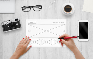 Leinwandbilder - Web designer draw layout of website on paper. Top view of work desk with computer, phone, camera, glasses, coffee.