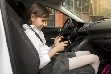 portrait of girl sitting in car and playing on smartphone