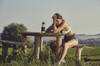 Exhausted female runner with hand on head resting on a rustic wooden bench. Pretty young woman having a headache from dehydration or overtraining. Young sporty lady having a bad training day.