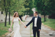 © olegparylyak - Beautiful couple of happy stylish newlyweds walking in the park on their wedding day with bouquet
