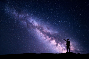Wall Mural - milky way with silhouette of a standing young man pointing finger in night starry sky on the mountai