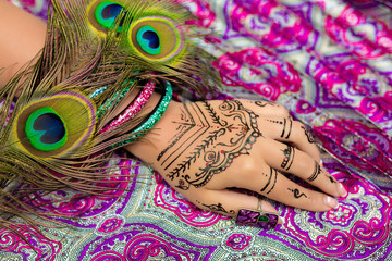 Women's beautiful hand with delicate fingers and a neat white lacquer manicures, henna with decorative elements. Indian oriental style, ornamental patterns. Luxury bracelets, green peacock feathers